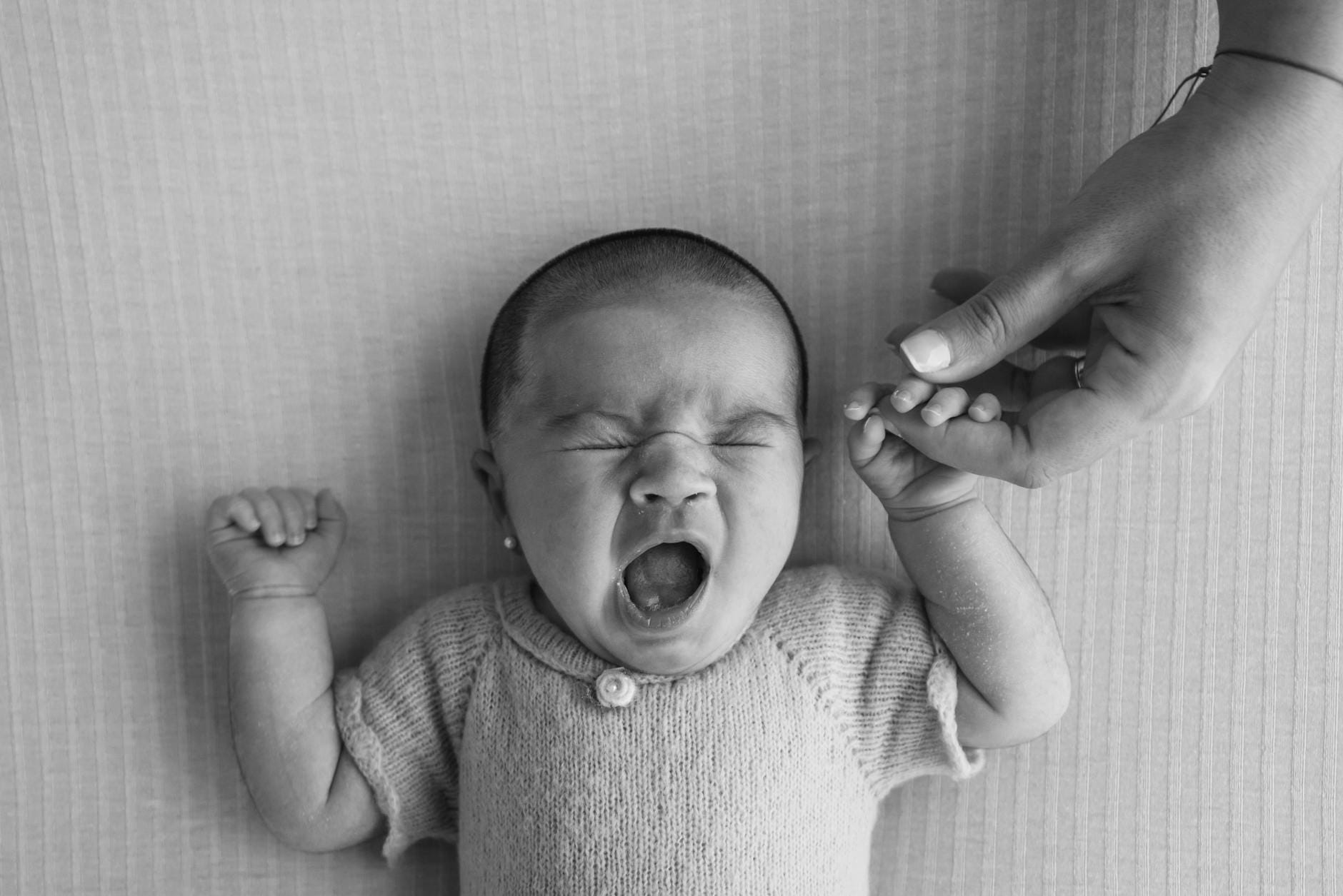 Ziewające noworodek trzymające dłoń dorosłego podczas zasypiania