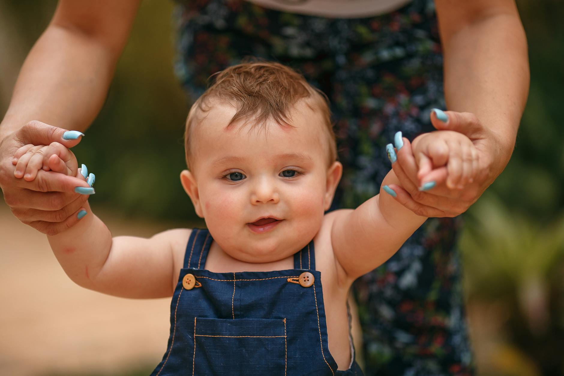 Małe dziecko stawiające pierwsze kroki na dworze z pomocą dorosłego