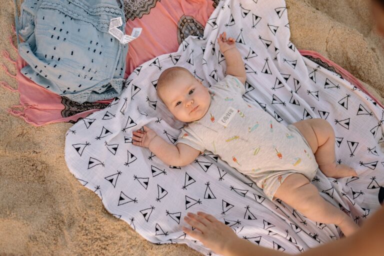 Niemowlę leżące na wzorzystym kocu na plaży w słoneczny dzień